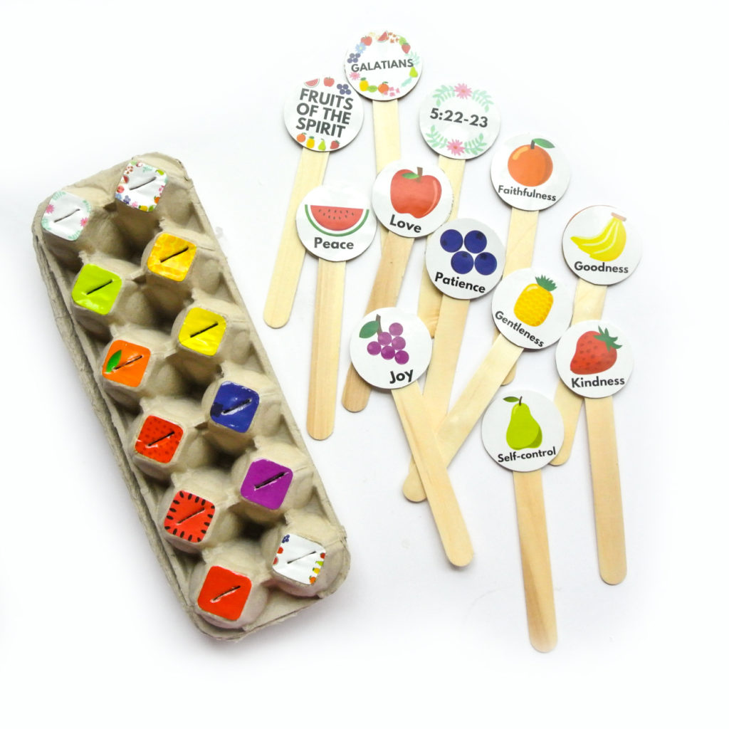 Egg carton with colored stickers and popsickle sticks with fruit graphics and fruits of the spirit labels for Toddler matching activity