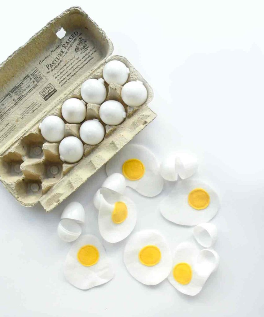 Shows carton of plastic white eggs with cracked opened egg shells and felt eggs on side