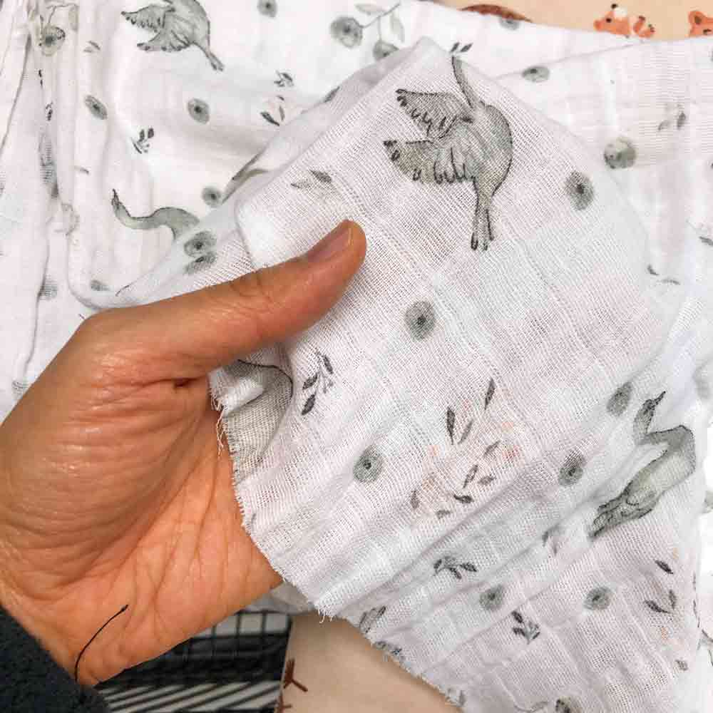 what fabric is best for baby bibs. Hand holding 100% printed cotton swaddle fabric up close image 