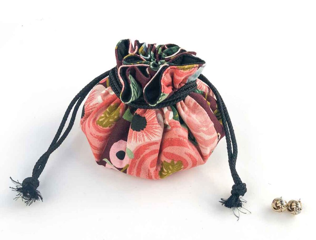 Drawstring jewelry bag with 8 pockets closed with a pair of earrings next to it