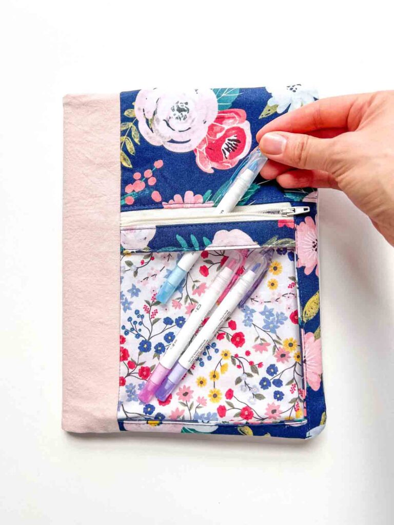composition notebook cover with zipper and clear vinyl pocket, with hand putting in a highlighter into the pocket. 