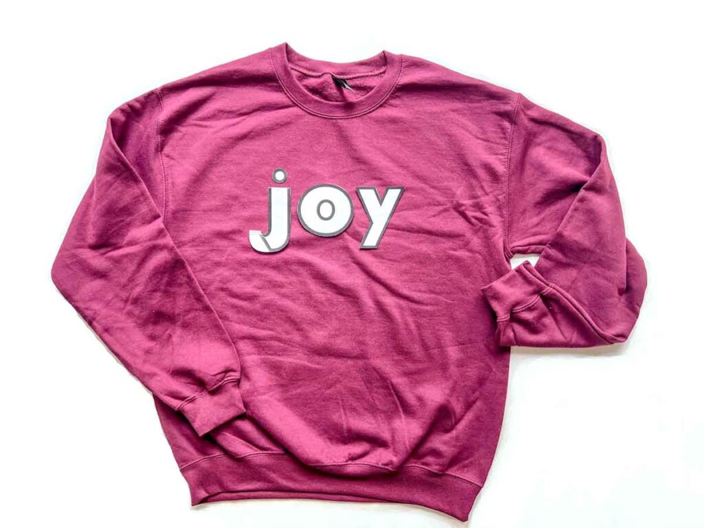 paper template cut out with letters 'joy' on top of plain sweatshirt