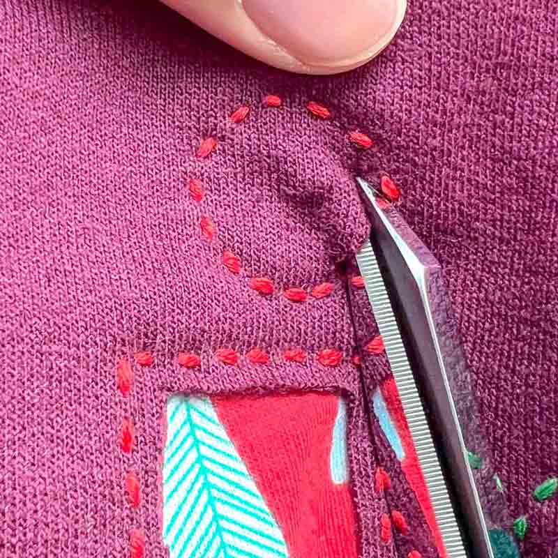 Carefully cutting away sweatshirt fabric around stitched reverse appliqué